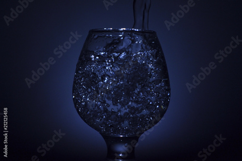 Simple still-life photo of whisky glass, water jet and dim colour light photo