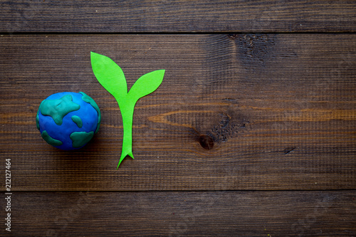 Planet, ecology. plastiline symbol of planet Earth globe and plant coutout on dark wooden background top view copy space