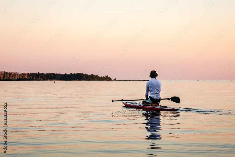 Paddle board rider at sunrise on calm water