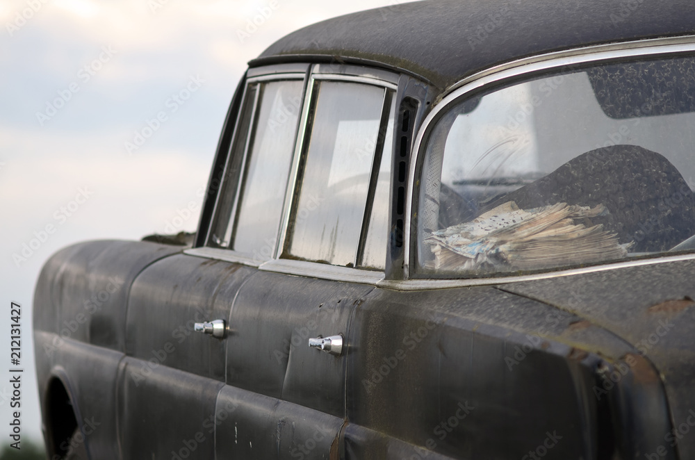Abandoned old black car. Close up. Side rear view with chrome handle and newspapers inside the car. Abandoned old black car. Close up. Side rear view with chrome handle and newspapers inside the car.