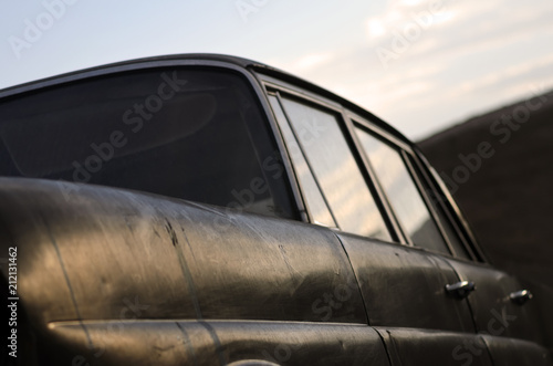 Abandoned old black car. Close up. Soft focus. Front view from below of an old car. In the foreground the fender and behind the side with reflection of sky in car windows. © Federico Barone