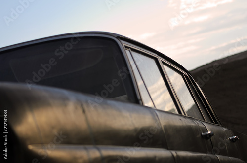 Abandoned old black car. Close up. Soft focus. Front view from below of an old car. In the foreground the fender and behind the side with reflection of sky in car windows. © Federico Barone