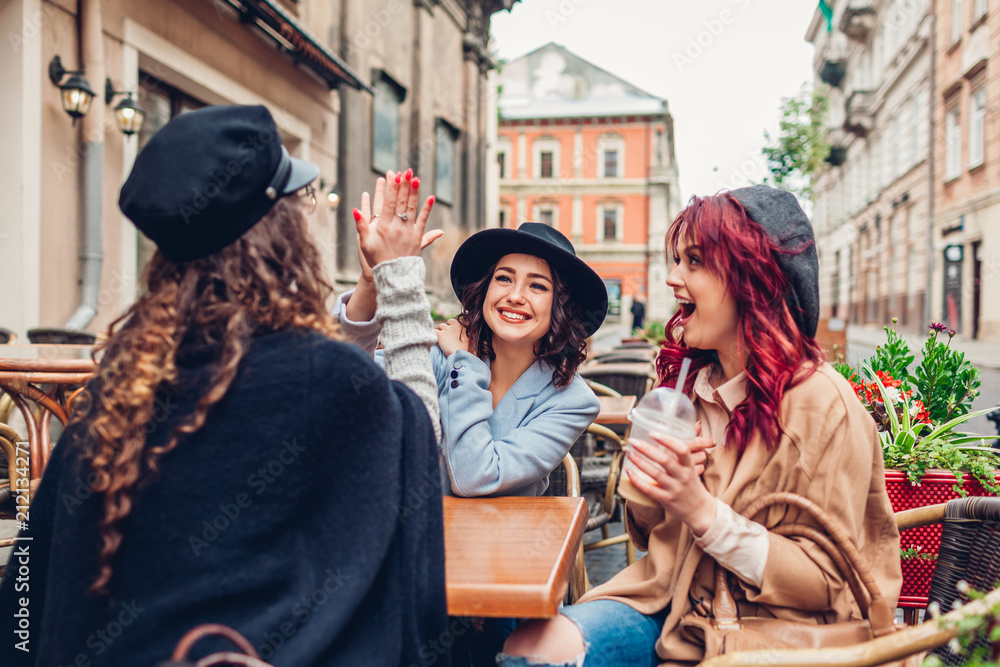Three female friends having drinks in outdoor cafe. Woman giving high five to her best girlfriend