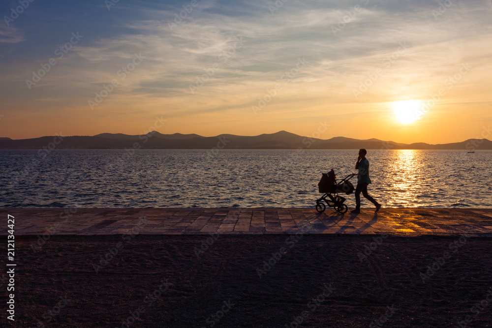 Young women strolls with baby carriage on Zadar waterfront in Croatia.