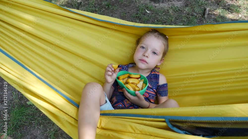 Lying in yellow hammock cute child girl have fun sway and eat summer fruits healthy food Lying in yellow hammock cute child girl have fun sway and eat summer fruits healthy food
