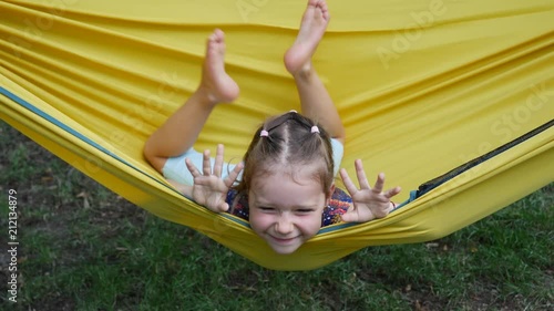 Girl child funny amuse enjoy lying in yellow hammock wagging barefooted legs smile