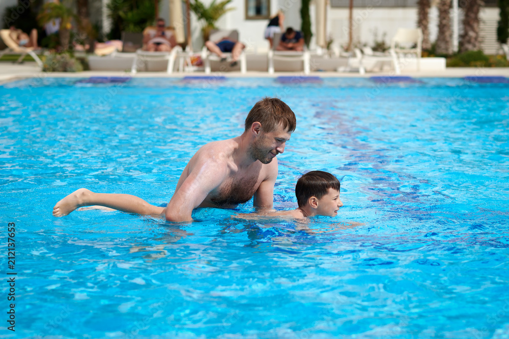 Cute caucasian boy is obtaining swimming skills. His father is helping him. Cute caucasian boy is obtaining swimming skills. His father is helping him.