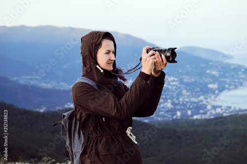 A girl traveler takes pictures at the top of a mountain. Sunset light, evening.
