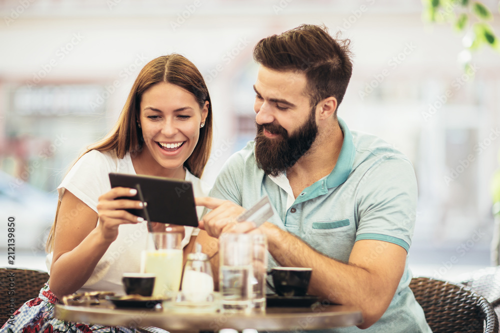 Beautiful couple having coffee on a date, using digital tablet and credit card for online shopping Beautiful couple having coffee on a date, using digital tablet and credit card for online shopping