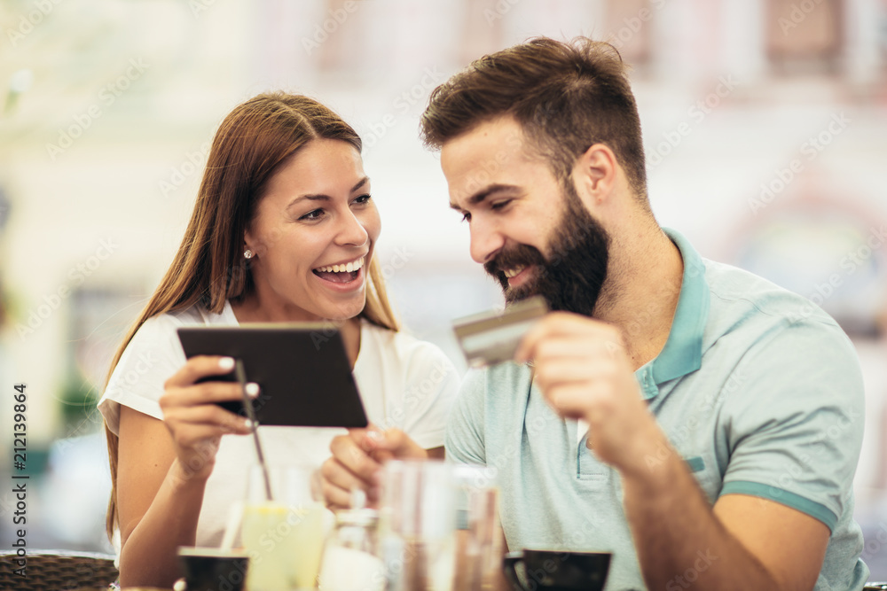 Beautiful couple having coffee on a date, using digital tablet and credit card for online shopping