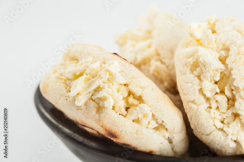 Colombian traditional white corn arepa stuffed with grated cheese in a black ceramic dish on black background