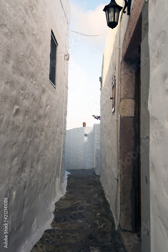 A view of a narrow street with arch and wooden windows and doors with white wall stone architecture of the island Patmos  Greece