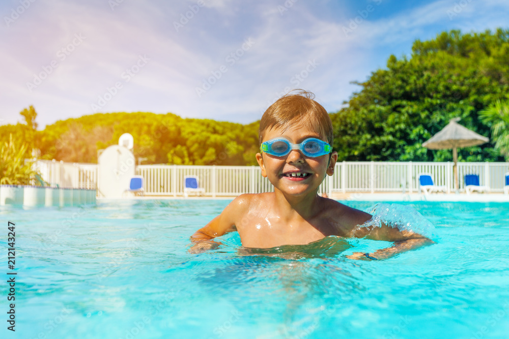Boy with swimming goggles standing in outdoor pool