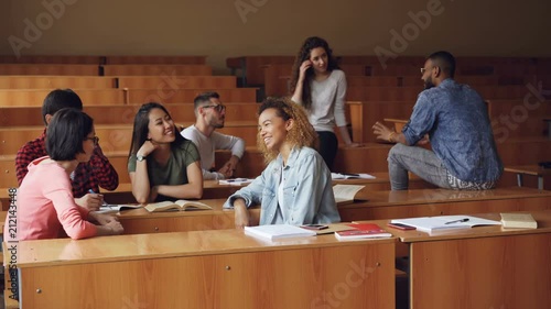 Multiracial group of students are relaxing and chatting during break enjoying free time and communication. Wooden tables, attractive people and noteboks are visible. photo