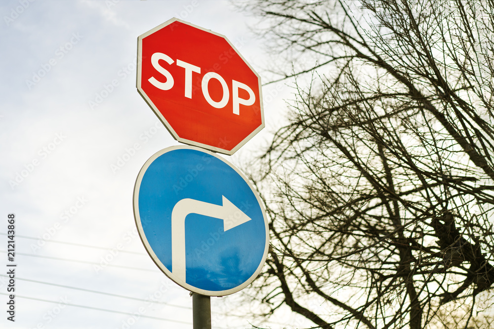 Stop sign and road sign turn to the right against a blue sky and a tree