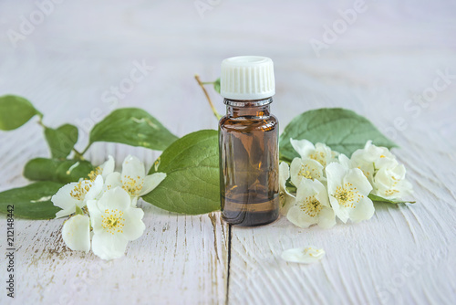 White flowers of jasmine (syringa) and little dark glass bottle on white paint wooden background