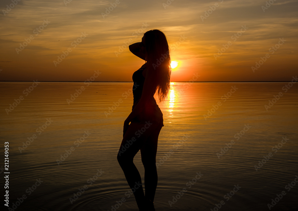 Beautiful young g in shorts stands by the sea on a sunset background, silhouettes