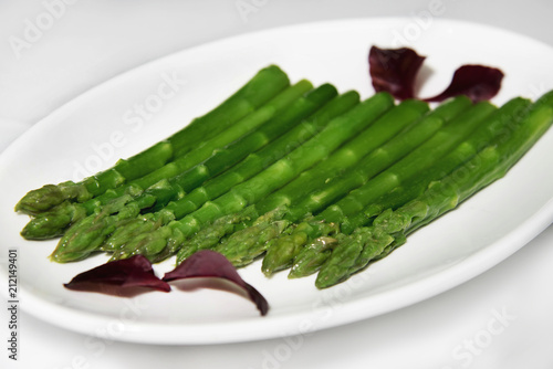 Green asparagus pods with basil leaves on a white plate.