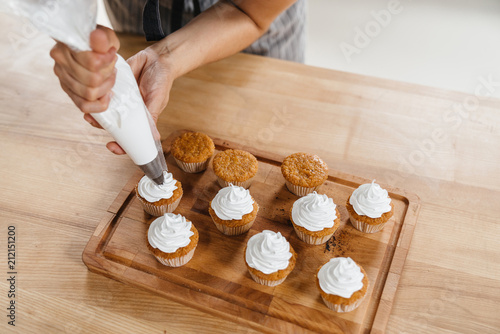 Confectioner woman decorates a capcake or muffin with whipped cream through a pastry bag. photo