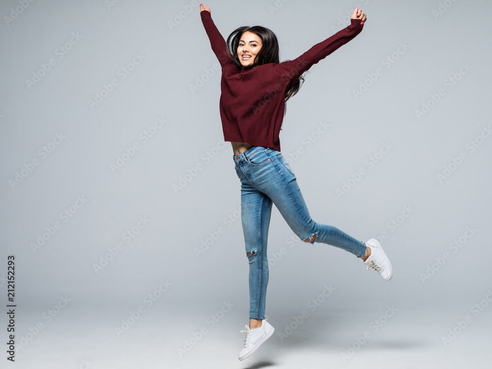 Happiness, freedom, power, motion and people concept. full length portrait of smiling young woman jumping with raised fists over grey background