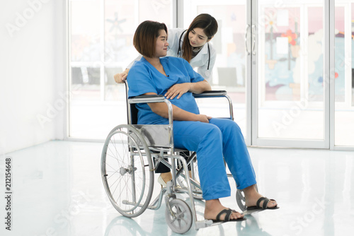 Asian woman Doctor talking to young pregnant woman in wheelchair at hospital. Beautiful asian doctor taking care of patient in wheelchair..