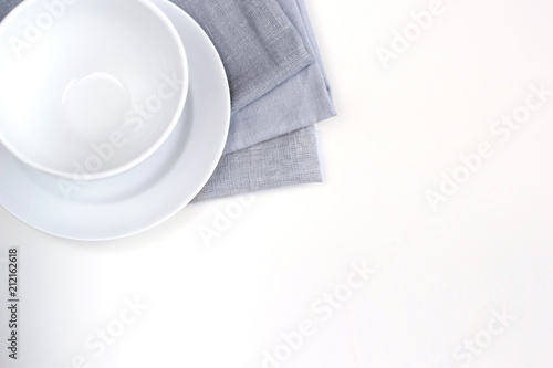 Empty white plate and bowl on a stack of gray napkins on a table.