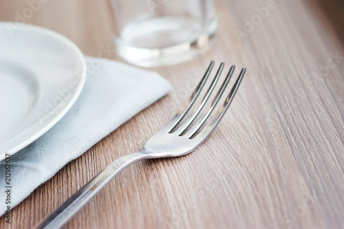 Empty white plate on a gray napkin with fork and glass on brown table. Table setting  preparation for meals.