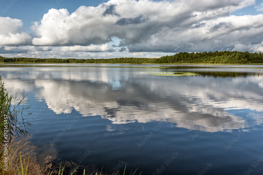 Fototapeta premium Quiet large lake with clouds reflected in the water, perimeter is guarded by a forest