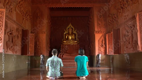 A woman and a man praying while kneeling in front of a Buddha statue in a Buddhist temple photo