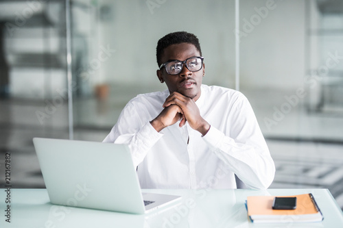 Serious black businessman thinking hard at business office desk, looking at papers. Busy, sitting, suit, hand on chin.