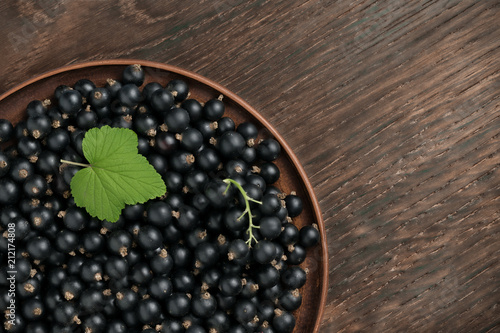 Harvest of black currant berries in a plate. Rustic wooden background