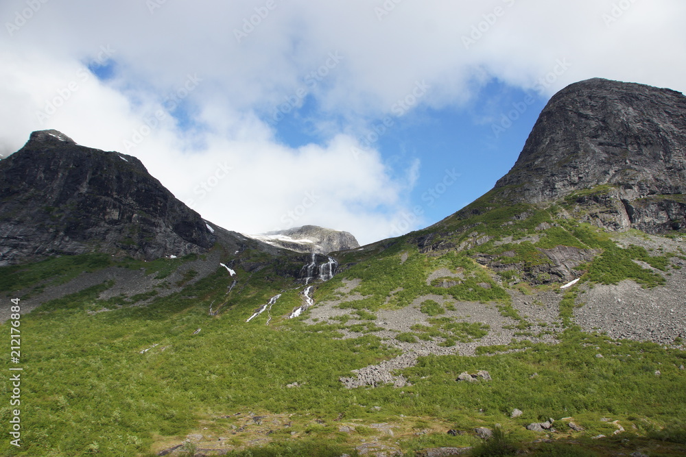 A small waterfall flows down the slope between the mountains in Norway in summer A small waterfall flows down the slope between the mountains in Norway in summer