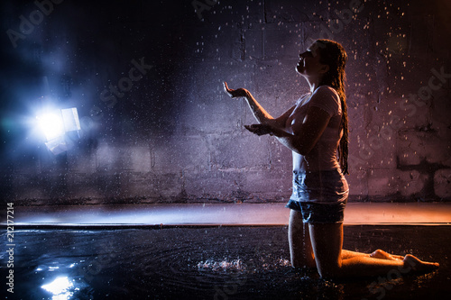 Girl with wet hair in the white shirt, water drops around and dark wall background illuminated by light