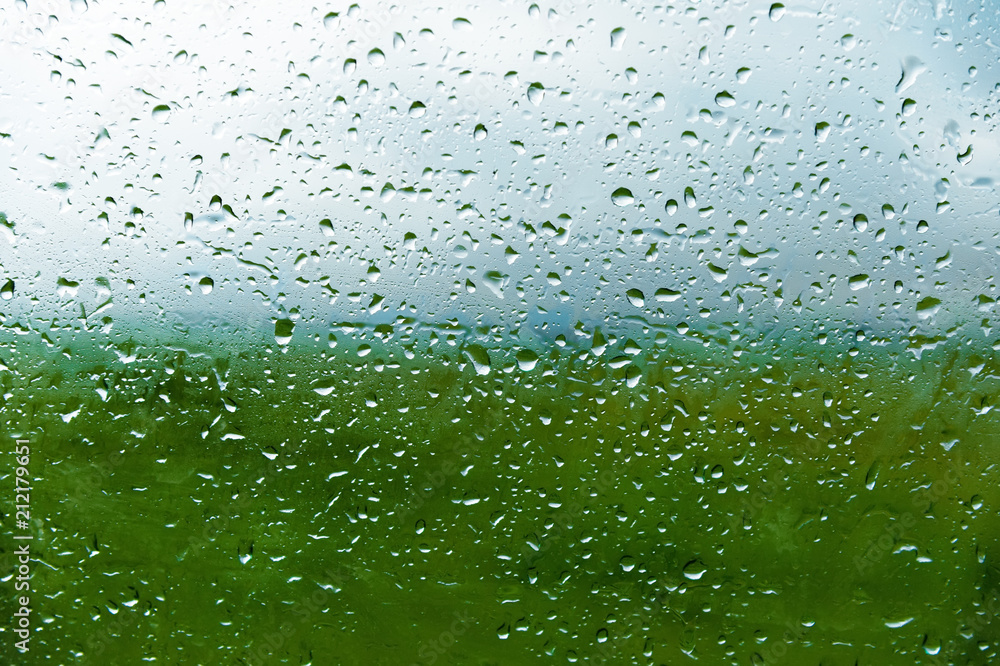 Natural background Drops on both sides of the glass from the rain and from the fogging abstract view, raindrops against the blue glass and the blurred landscape of the gradient of blue and green Natural background Drops on both sides of the glass from the rain and from the fogging abstract view, raindrops against the blue glass and the blurred landscape of the gradient of blue and green