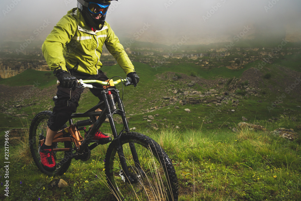 Naklejka premium A man in a mountain helmet riding a mountain bike rides around the beautiful nature in cloudy weather. downhill