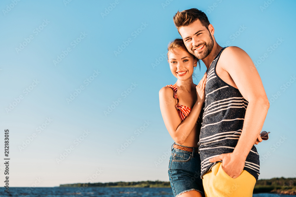 beautiful happy young couple smiling at camera while standing together on beach beautiful happy young couple smiling at camera while standing together on beach
