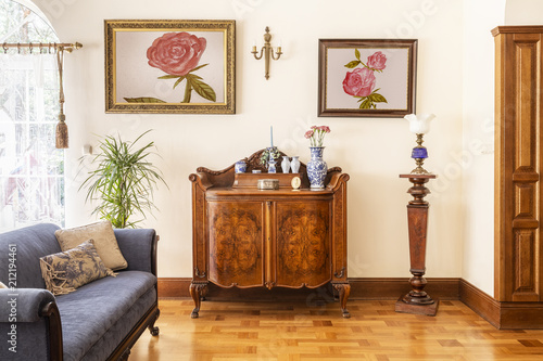 Posters of roses above wooden cabinet in elegant living room interior with blue sofa. Real photo