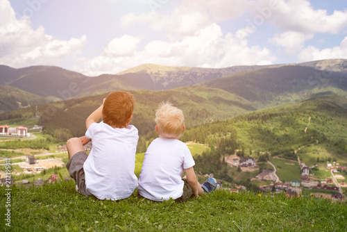 Two boys sitting on a hill and looking at the mountains. Back view