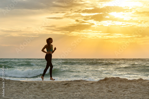 Girl in sportswear running along the surf line. Early morning.