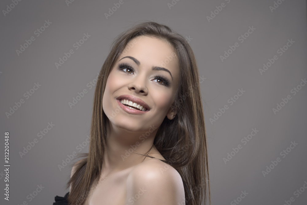 Stunning mixed race brunette beauty with perfect smile looking up at copyspace and smiling over gray background. 