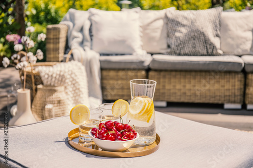Fruits and glass with water on rattan table on the terrace with settee and flowers. Real photo