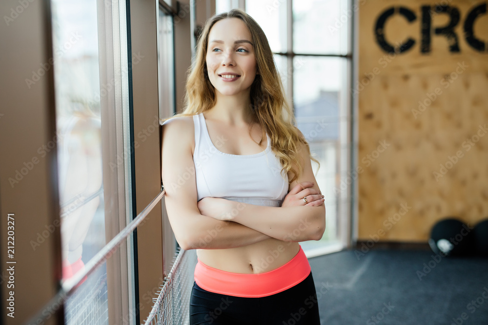 Portrait of positivity and pretty girl smiling at camera and posing with crossed arms in the gym.