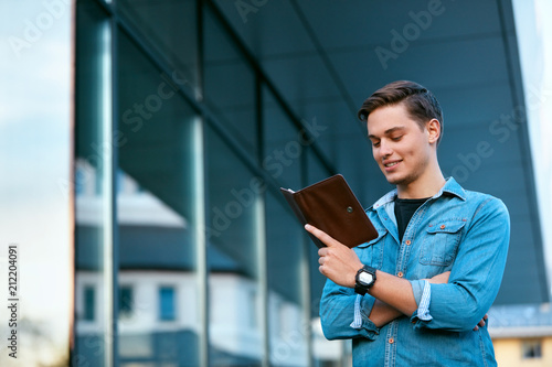 Male Student Reading Book Outdoors At College