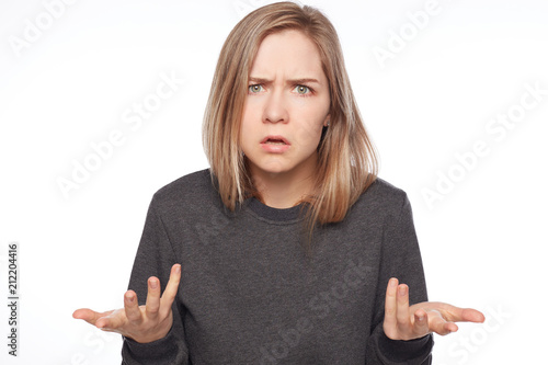 Portrait of furious young Caucasian female gestures in anger, being dissatisfied with results of work, screams loudly. Frustrated blond haired lady full of rage gestures against white studio wall.