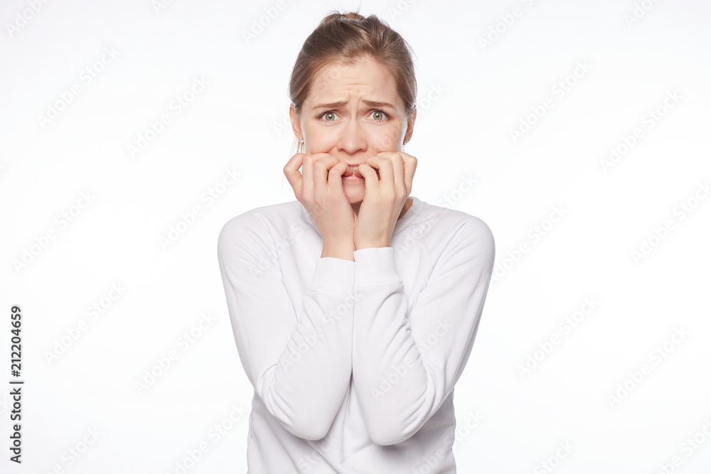 Woman is very terrified, trembling from fear. Portrait of attractive blond European female, biting fingernails and frowning, being worried and nervous, seeing something scary over white background. Woman is very terrified, trembling from fear. Portrait of attractive blond European female, biting fingernails and frowning, being worried and nervous, seeing something scary over white background.