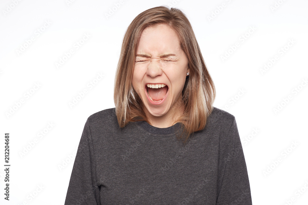 Close up of attractive blond Caucasian female yelling loudly, keeping mouth wide opened, expressing negative emotions, producing loud sound, isolated on white background. Annoyed angry woman screams. Close up of attractive blond Caucasian female yelling loudly, keeping mouth wide opened, expressing negative emotions, producing loud sound, isolated on white background. Annoyed angry woman screams.