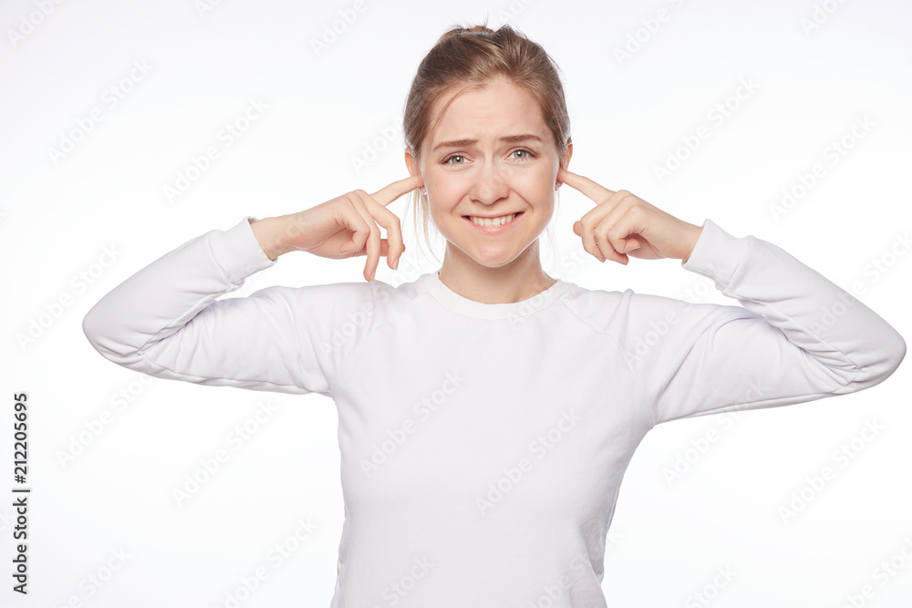 Turn off annoying sound, lady needs silence. Indoor shot of bothered and distracted charming female shutting ears with index fingers, looking at camera with displeased expression, hearing loud noise. Turn off annoying sound, lady needs silence. Indoor shot of bothered and distracted charming female shutting ears with index fingers, looking at camera with displeased expression, hearing loud noise.