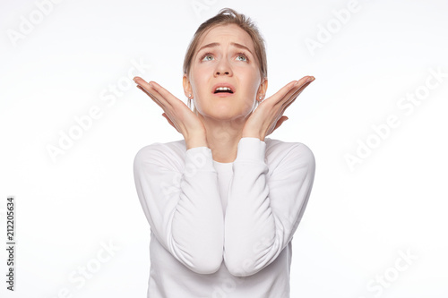 God please. Close up isolated portrait of young unhappy Caucasian female student dressed in white jumper holding palms up, looking up with worried expression, asking why and begging for happy end.