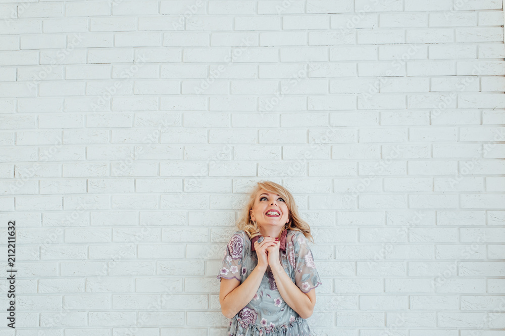 Blonde happy woman in light dress with stay in front of light wall