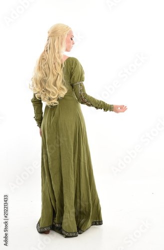 full length portrait of blonde girl wearing green medieval gown, standing pose facing away from camera. isolated on white studio background.